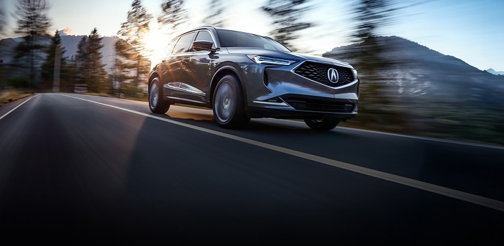 2024 Acura MDX Advance Package in Liquid Carbon Metallic front driving on a scenic road (Premium Performance SUV). 2024 Acura MDX Advance Package in Liquid Carbon Metallic front driving on a scenic road (Premium Performance SUV).